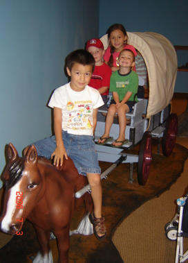 LaurenBlackburn_family.jpg Four children sit on a kid-size covered wagon; one of them sits on the plastic horse in front.