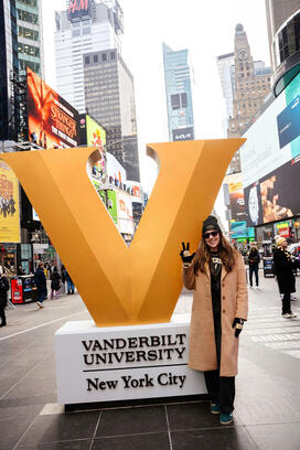 Stephanie Burset stands next to a giant V for Vanderbilt University in what looks like Times Square.