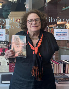 Constance Escher stands in the entry of the Princeton Public Library and is holding a copy of her book.