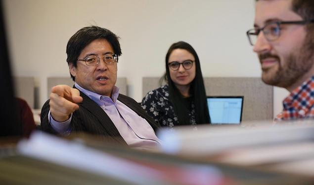 Professor Sam Wang points toward the camera; he's in a room where students sit at computers but look at him.