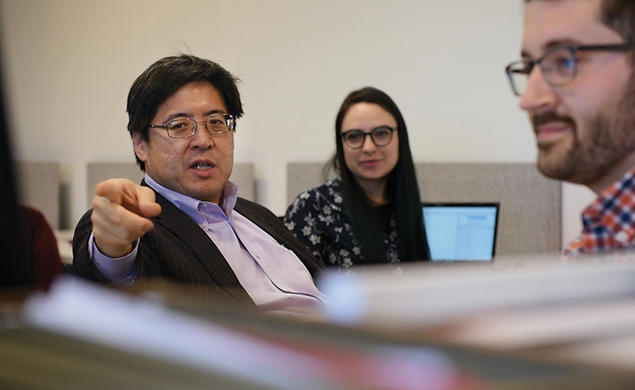 Professor Sam Wang points toward the camera; he's in a room where students sit at computers but look at him.