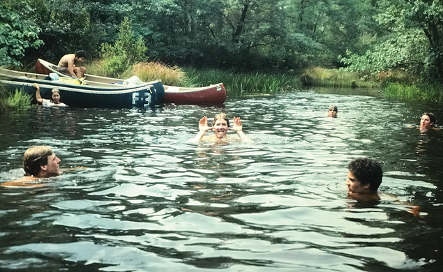 Students swimming in a river with canoes on the bank