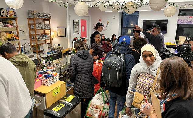 People pack into the Little Shop of Kindness; round paper lanterns and an ivy garland hang overhead.