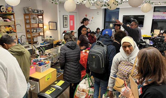 People pack into the Little Shop of Kindness; round paper lanterns and an ivy garland hang overhead.