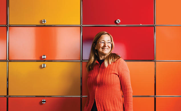 Kim Scott stands against a wall of yellow, orange, and red cabinets.