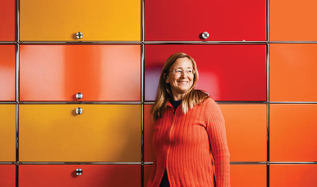 Kim Scott stands against a wall of yellow, orange, and red cabinets.