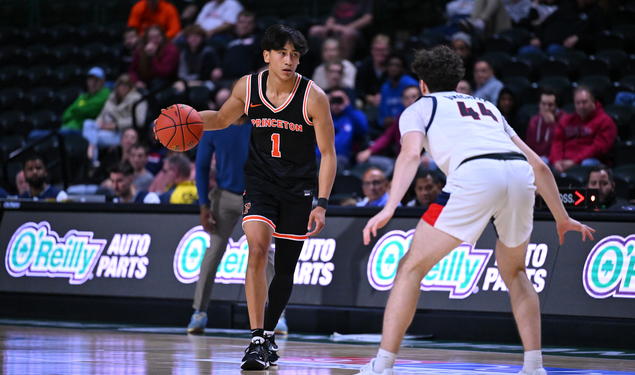 A basketball player wearing a Princeton jersey with a #1 on it, dribbles while facing off a defender.
