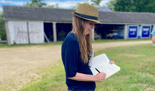 Michelle Lerner writes in a journal outdoors, a barn in the background.