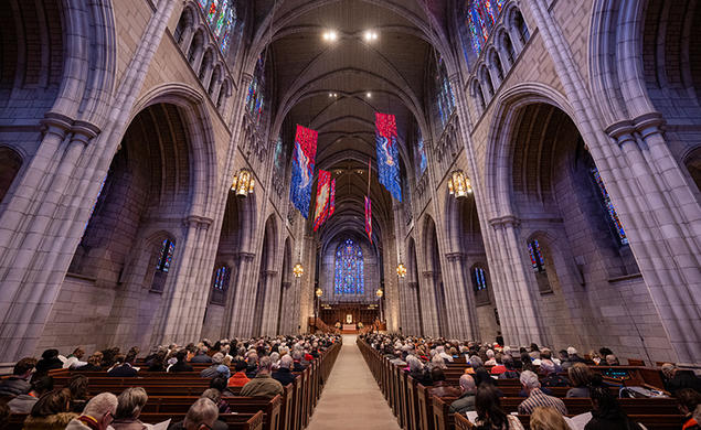 View down the aisle of the Gothic University Chapel, flanked by stone arches and full of people in the pews.