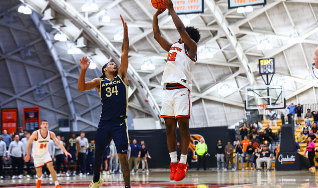 Princeton basketball player Dalen Davis '27, jumps while preparing to shoot a three. A player from Akron is jumping in front of him, attempting to block the shot. 