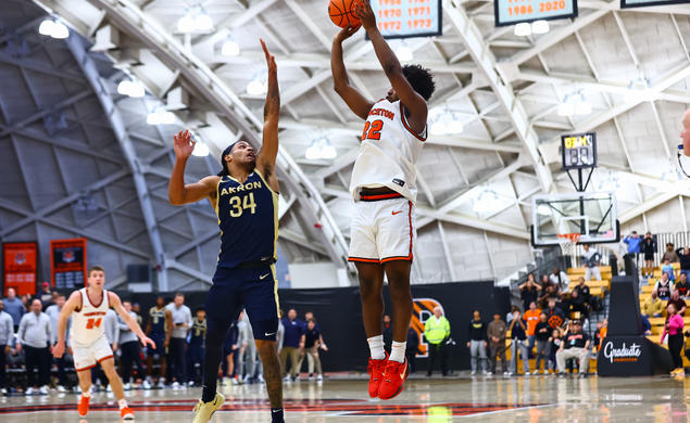 Princeton basketball player Dalen Davis '27, jumps while preparing to shoot a three. A player from Akron is jumping in front of him, attempting to block the shot. 