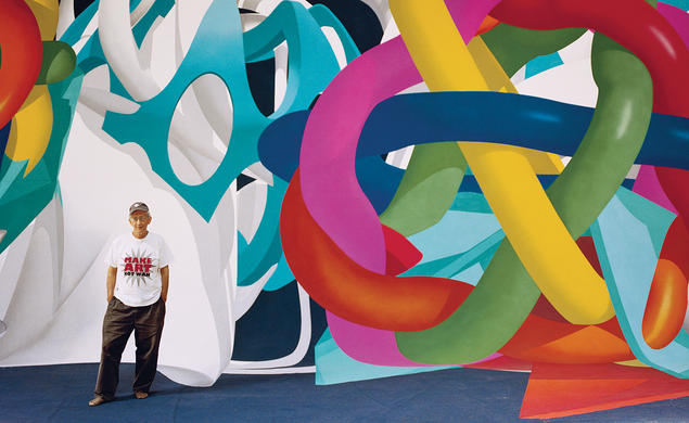  Frank Stella wearing a Make Art Not War t-shirt standing in front ofa huge colorful painting