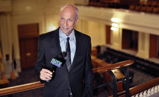 Michael Aron *70 holds a microphone while speaking from an upper level of the NJ statehouse.