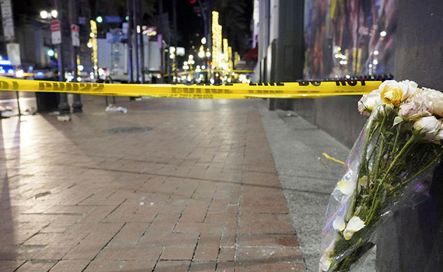 At night, a bouquet of flowers leans up against a building next to a brick sidewalk blocked off with caution tape.