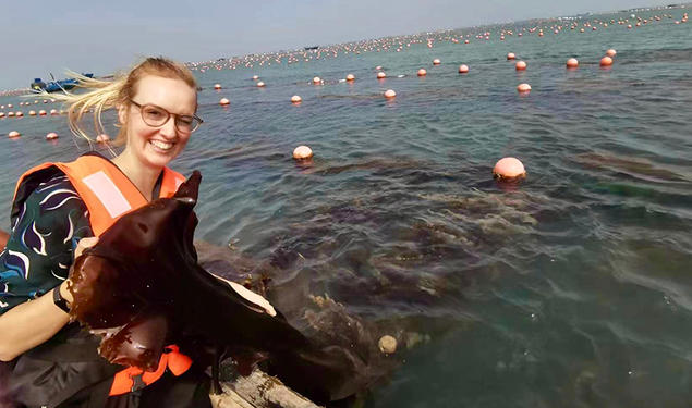 Helen Park sits in a boat holding a piece of kelp.