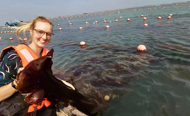 Helen Park sits in a boat holding a piece of kelp.