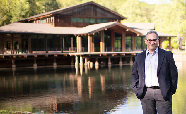 Jason Posnock ’94 stands in front of a pond and a rustic-looking building at the Brevard Music Center.