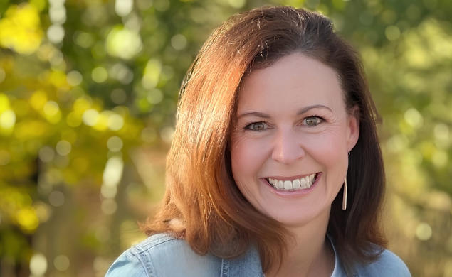 Andi Almond smiling for a photo with greenery in the background.