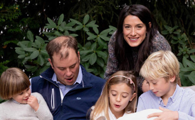 Milano Buckley looks up and smiles in a family photo where her husband and three children are all looking down.