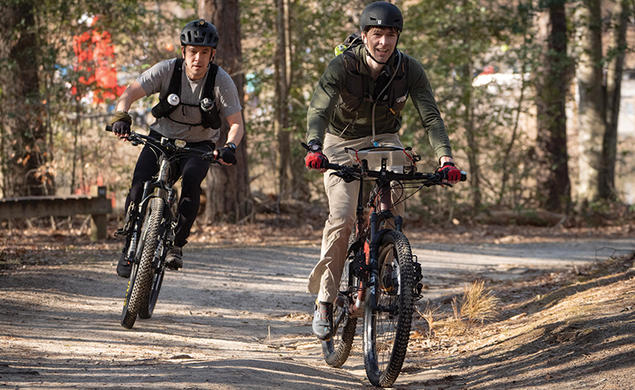 Two men ride bicycles.