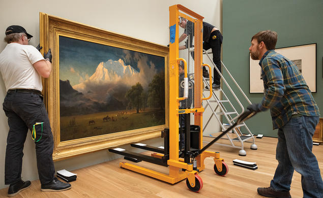 Two men move a large painting of a landscape into the new art museum. 