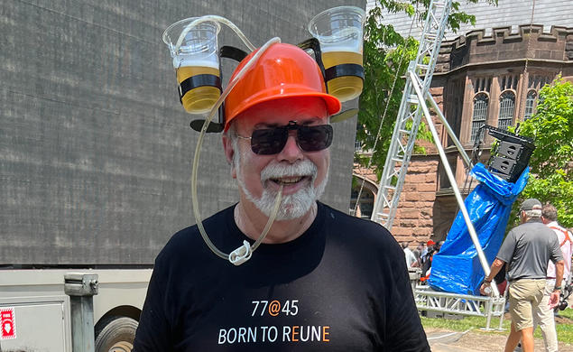 A man wears a hard hat with two cups of beer attached. His shirt reads "Born to Reune."