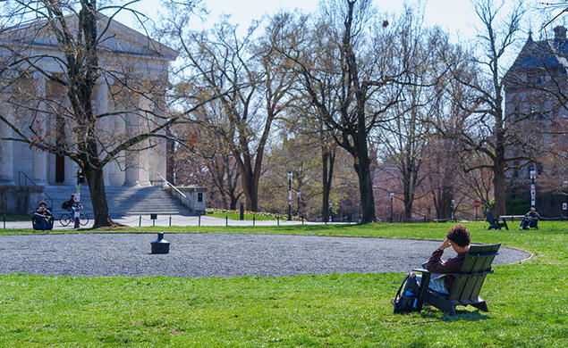 A student sits in an Adirondack chair facing away from the camera and toward Cannon Green, where the top of a buried canon is visible.