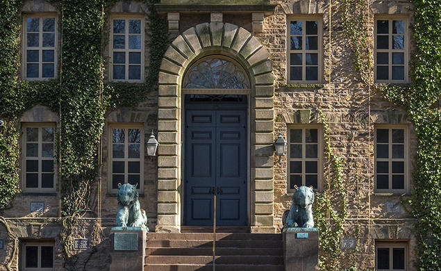 The front door to a stone building with paned windows, a stone archway over the door, and bronze tiger statues one each side.