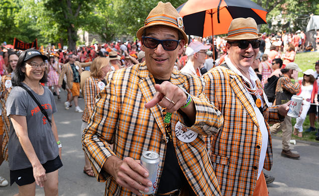 A man in an orange plaid blazer points to the camera during the P-rade.