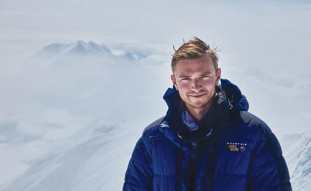 Ben Weissenbach in a blue puffer jacket on top of a snow covered mountain