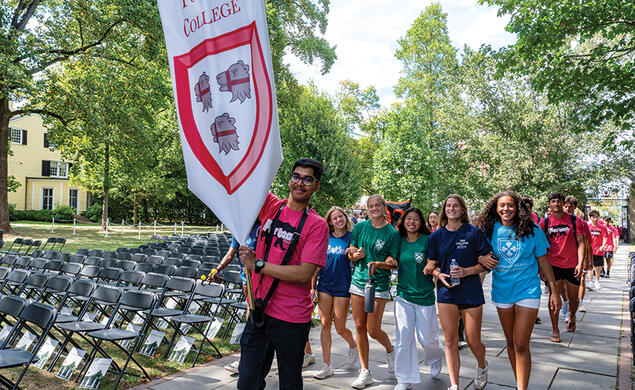 Students marching; one at the front carries a red-and-white "Forbes College" banner.