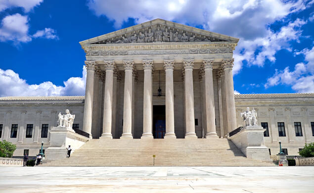 Front view of the U.S. Supreme Court building which is white stone and a staircase leading up to the eight pillars.