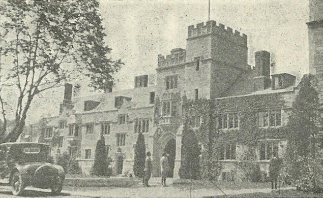 Black and white photo of a Gothic campus building, with an old-fashioned car parked in front.