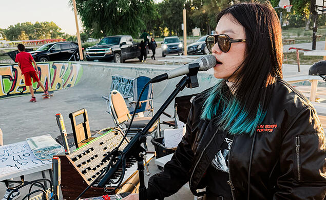 A woman sings into a microphone in a skate park.