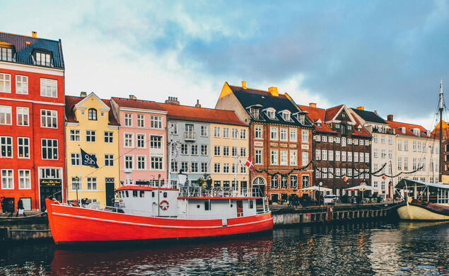 Row of colorful houses behind a a red boat behind a body of water. 