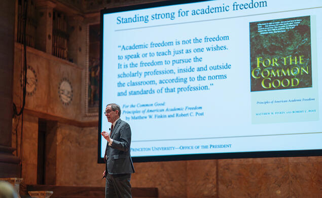 President Eisgruber speaks in front of a screen with a presentation about academic freedom.