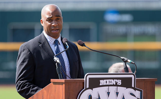 Damani Leech ’98 speaks at a podium with a baseball field in the background.