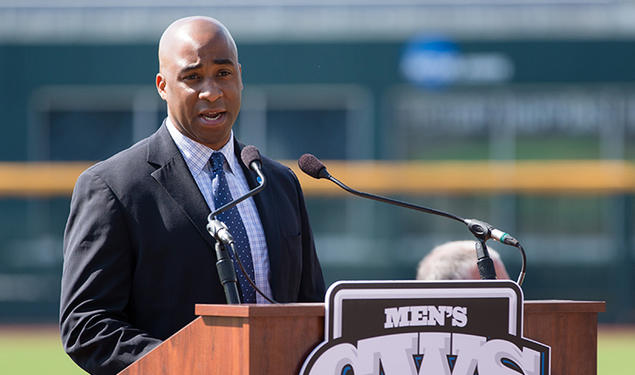 Damani Leech ’98 speaks at a podium with a baseball field in the background.