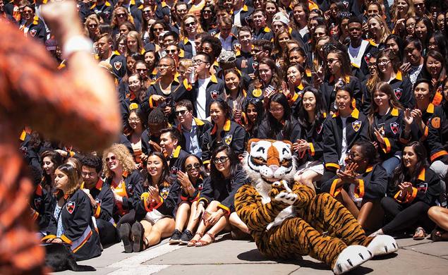 The Class of 2017 gathers in their black jackets behind the Tiger mascot, who's sitting on the ground and clapping his paws.