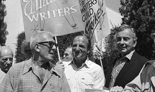 Black-and-white photo of three men in a crowd holding signs reading "Academy Award writers" and "The Writers Guild Strikes."