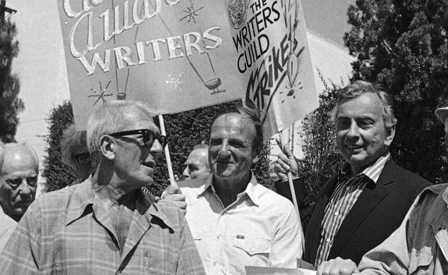 Black-and-white photo of three men in a crowd holding signs reading "Academy Award writers" and "The Writers Guild Strikes."
