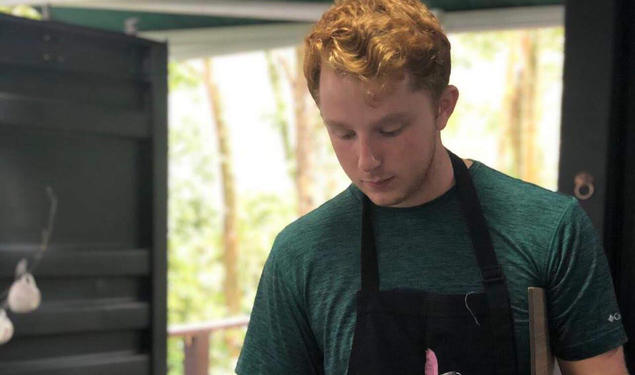 Alex Kaplan ’21 wears a black apron and holds a stainless steel container as he pours coffee into teacups.