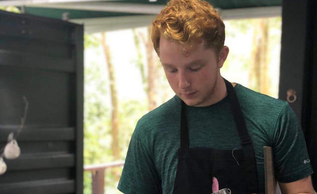 Alex Kaplan ’21 wears a black apron and holds a stainless steel container as he pours coffee into teacups.