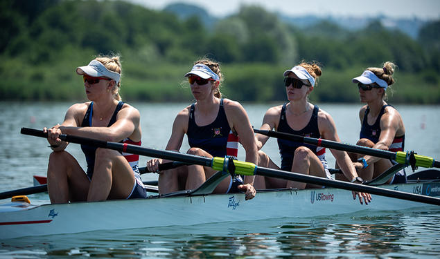 Four rowers at rest in a rowing shell on the water. Claire Collins is at left.