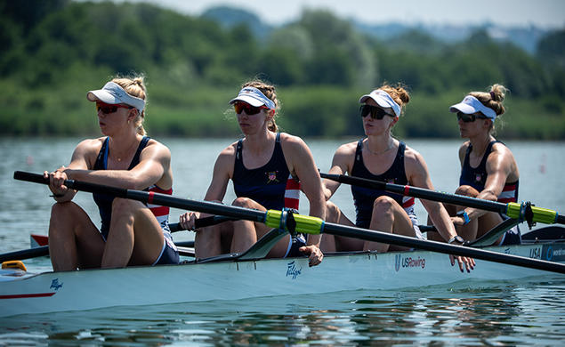 Four rowers at rest in a rowing shell on the water. Claire Collins is at left.