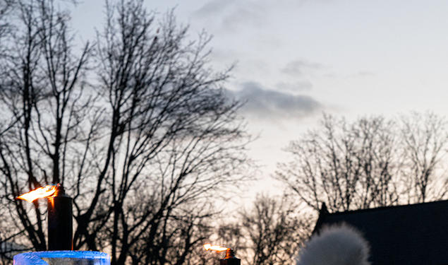 A view of the ice menorah showing it's about as tall as the person standing beside it in a winter hat.