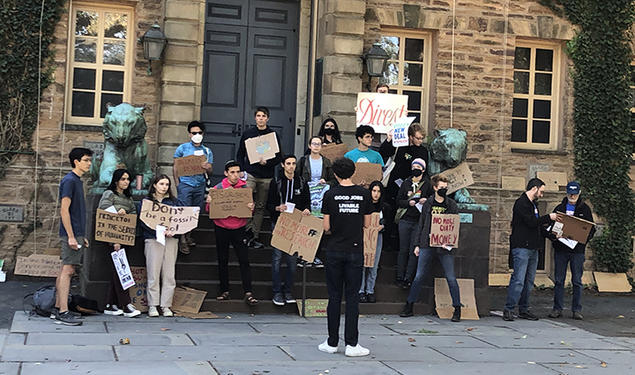 Students with Divest Princeton hold signs in front of Nassau Hall, made of cardboard and showing their support for Princeton divesting from fossil fuels.