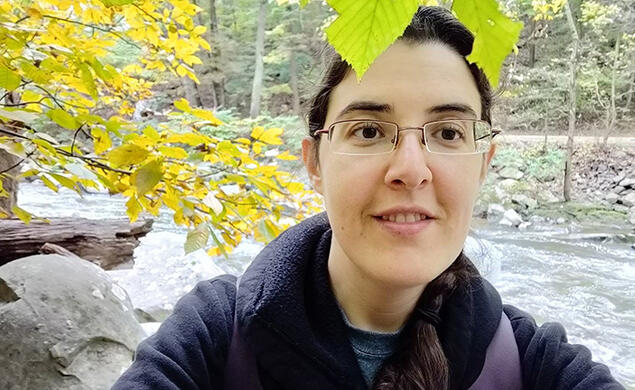 ElizabethTrees_cropped.jpg Elizabeth Tsurkov takes a selfie under a tree with a small river behind her.