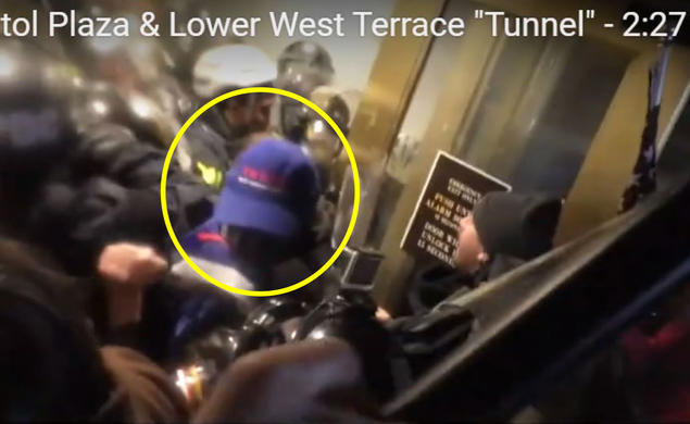 Someone with a blue baseball cap is seen near doors; people in riot gear are in the background.