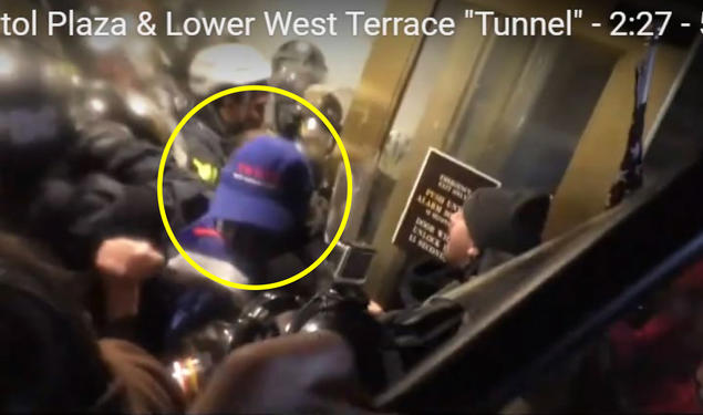 Someone with a blue baseball cap is seen near doors; people in riot gear are in the background.